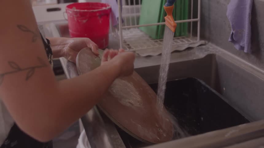 Female potter reclaims waste clay before washing the rest from a work disk in the sink