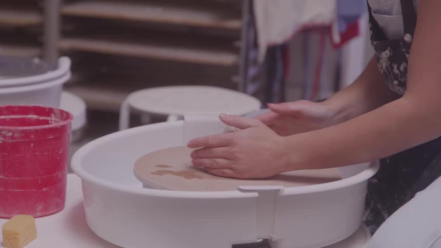Hands shaping a wet clay block on a pottery wheel