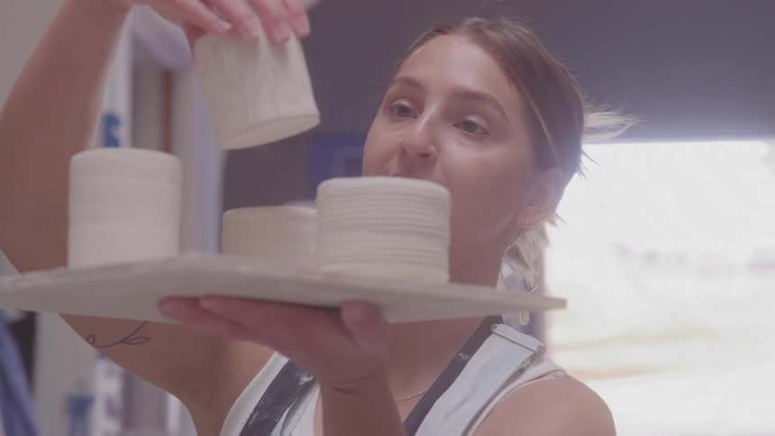 Female potter examines unfired clay cups while standing in her workshop