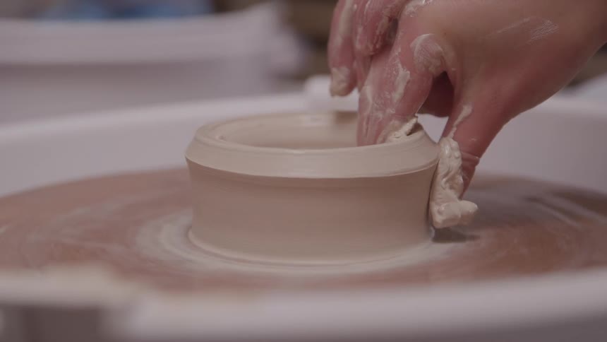 Female potter shapes a clay cup on a potters wheel