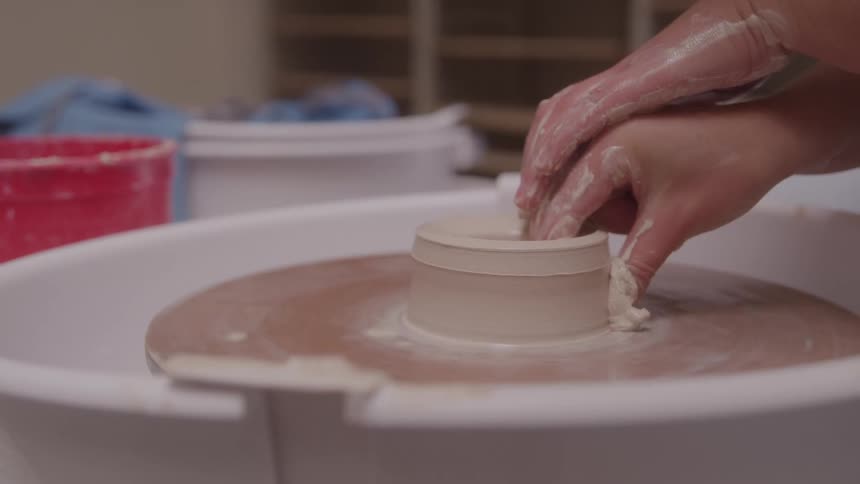 Woman using her hands to form a cup from clay on a pottery wheel