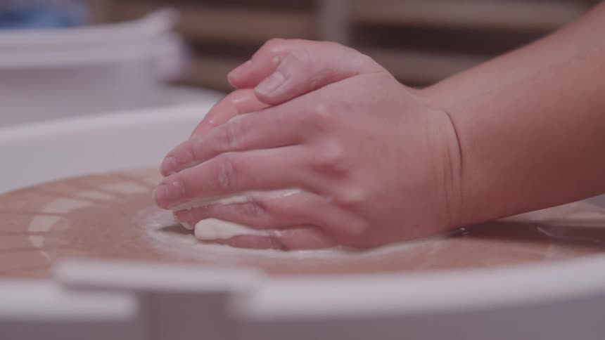 The woman is sculpting clay on a pottery wheel
