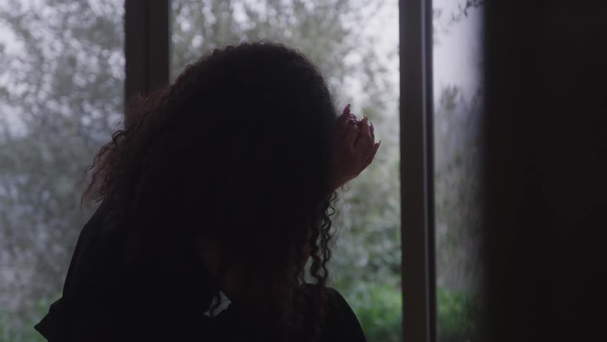 The woman sitting in the dark room is sad