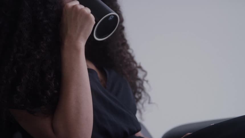 A young woman wearing a black tshirt drinks from a coffee mug indoors at midday