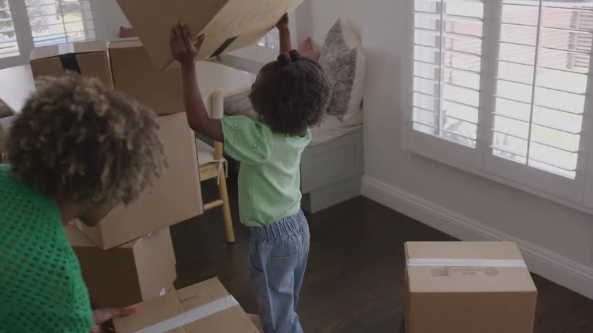 Child stacking a cardboard box in a room during a move
