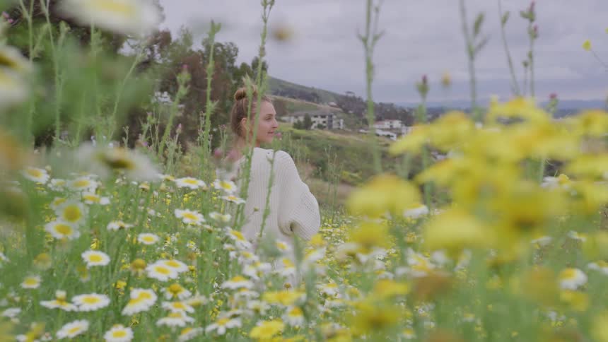 A young woman sits in a field of wild daisies on a hillside