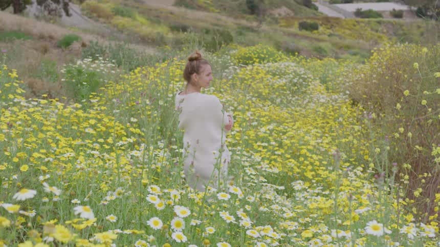 A woman is standing in a field of wildflowers on a mountain