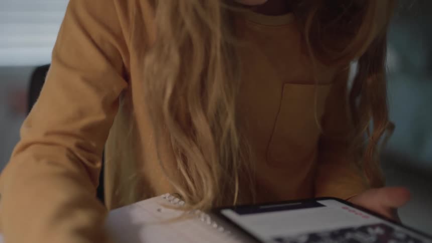 Girl references a tablet while working on homework during the daytime