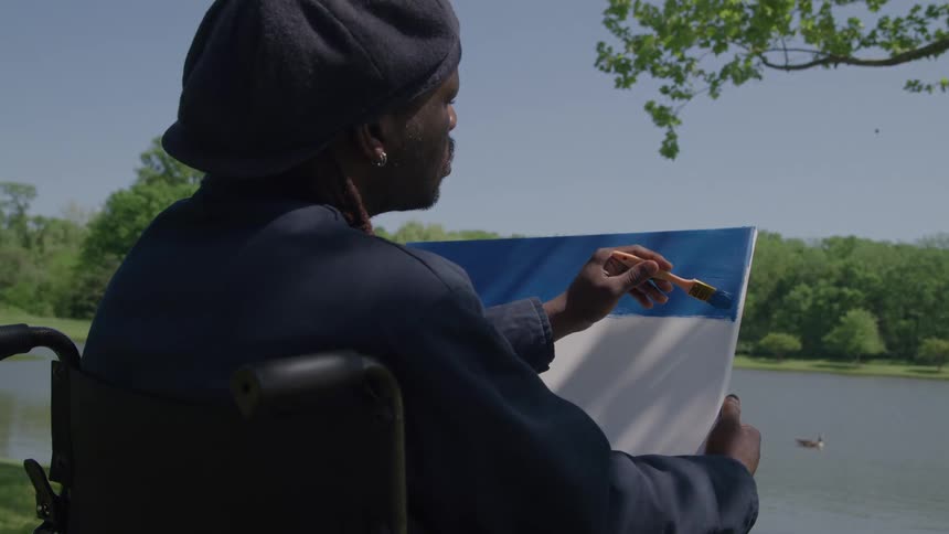 A man wearing a black beret is painting a white canvas blue
