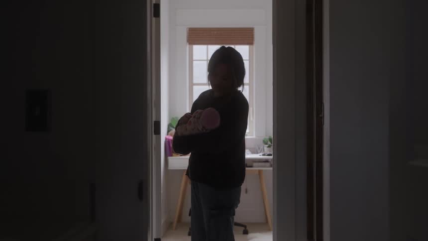 Woman standing in the hallway of her home rocking her baby in her arms