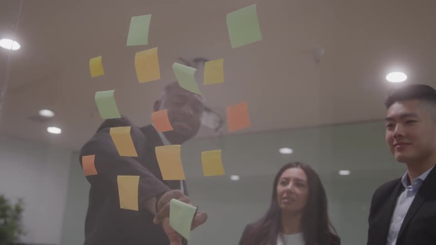 Team placing colorful sticky notes on a glass wall during a meeting