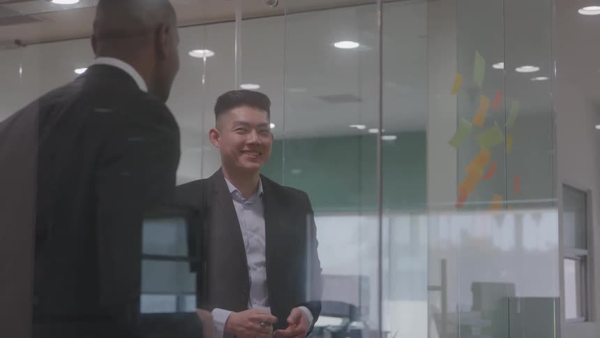 Men talking in front of a glass wall with colorful sticky notes in an office