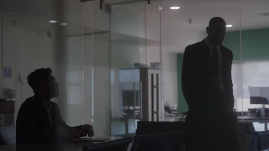 Men in a meeting inside a glasswalled room with dim lighting