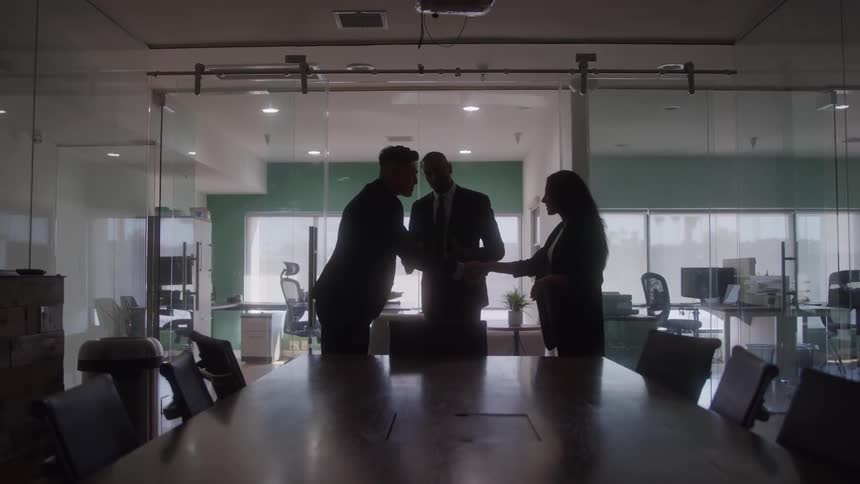 People standing in an office sand next to a table shaking hands and talking