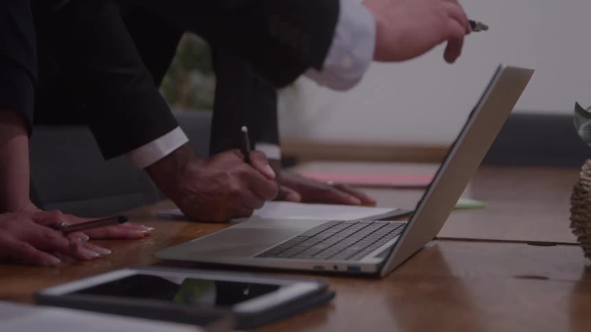 People in an office meeting stand over a laptop computer pointing at the screen