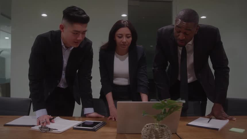 Three coworkers talk and look at a laptop in the office