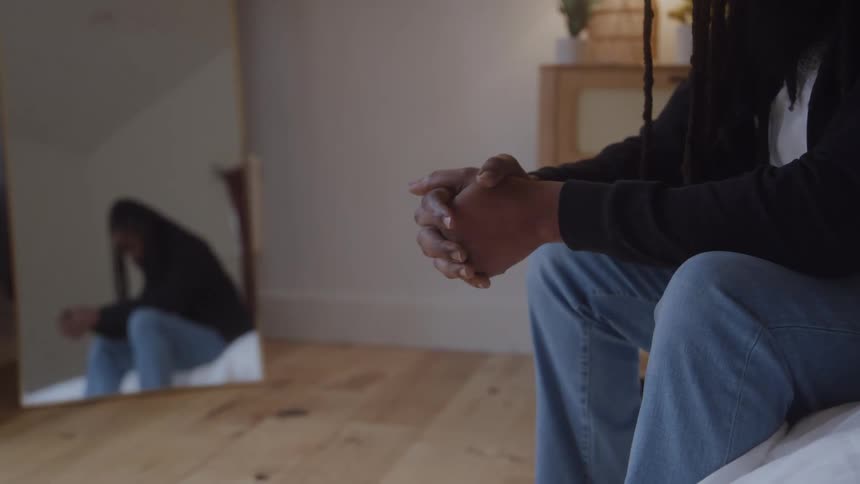 Man sitting with clasped hands reflected in a mirror in the bedroom