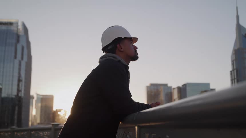 The construction worker is watching the sun rise in the city