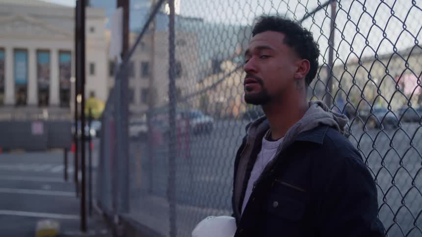 A man leans against a chain link fence