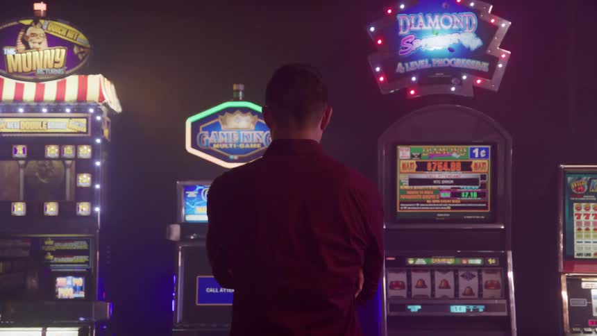 A man standing in front of a slot machine staring as the machines lights blink inside a casino