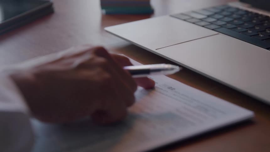 Office worker reads an income tax form while sitting at a desk holding a laptop computer
