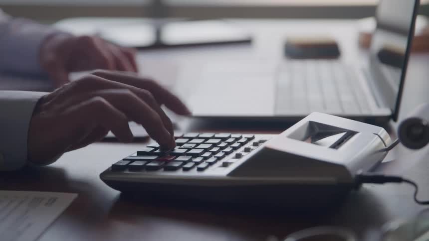 A persons fingers typing on the buttons of a calculator that is on a table