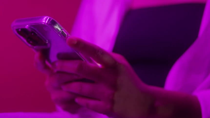 Hands holding a smartphone illuminated by bright pink light