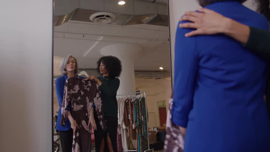 Woman helping a client choose a dress in front of a mirror
