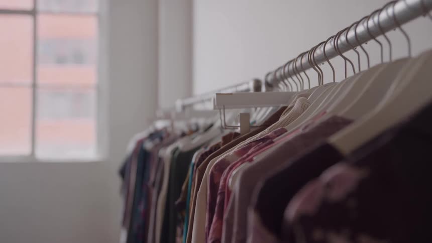 Clothes on hangers hang on a rack next to a wall