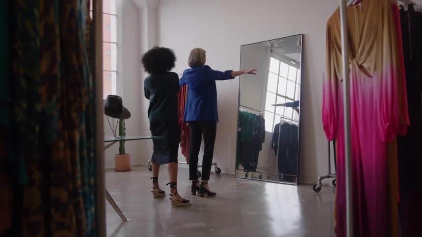 Woman measuring the arms of another woman trying on clothes in front of a mirror