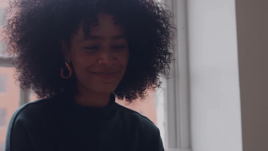 Woman smiling softly near a bright window
