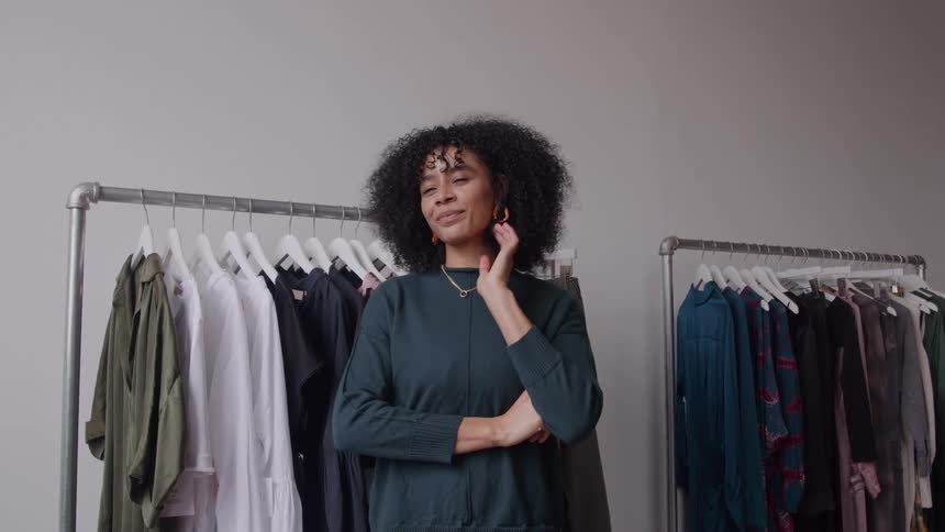 A woman with frizzy black hair stands in front of some clothing racks