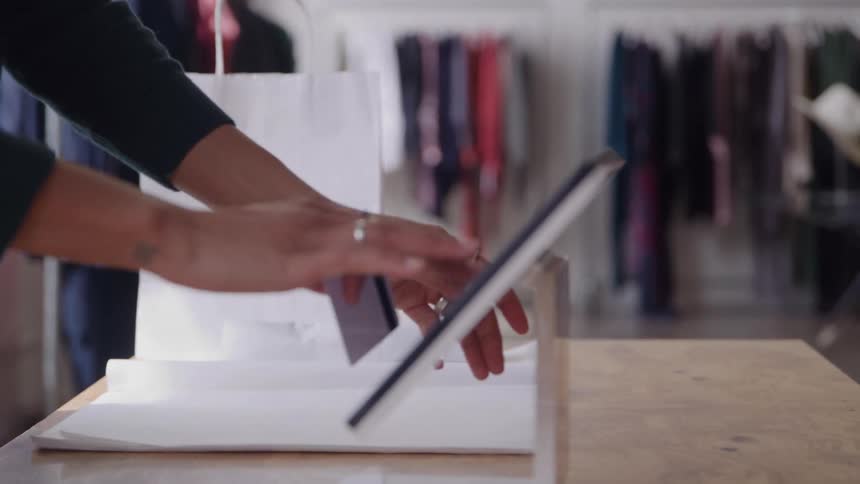Person hands another a card which is then placed on a tablet for payment in a clothing store