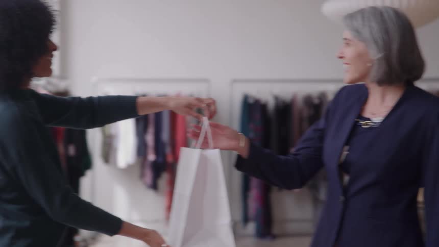 Clerk hands a bag to a shopper in a clothing store