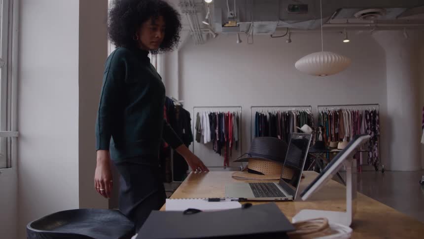 Woman sits and types on a laptop on a table in a fashion studio