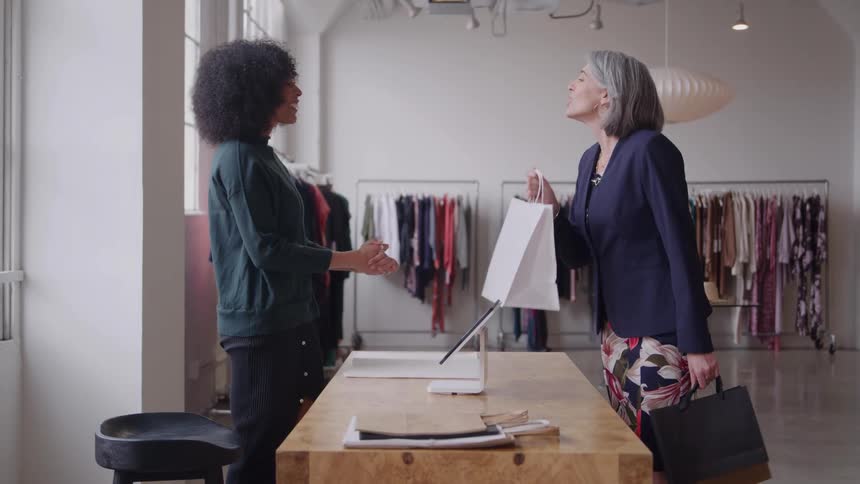 Woman handing a shopping bag to a customer in a fashion studio