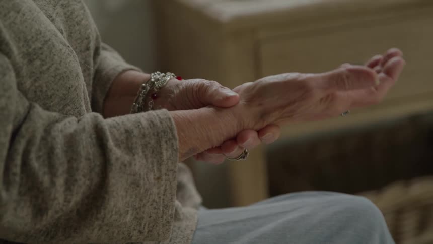 A closeup shot focuses on an elderly womans hands as she holds one wrist and flexes her fingers