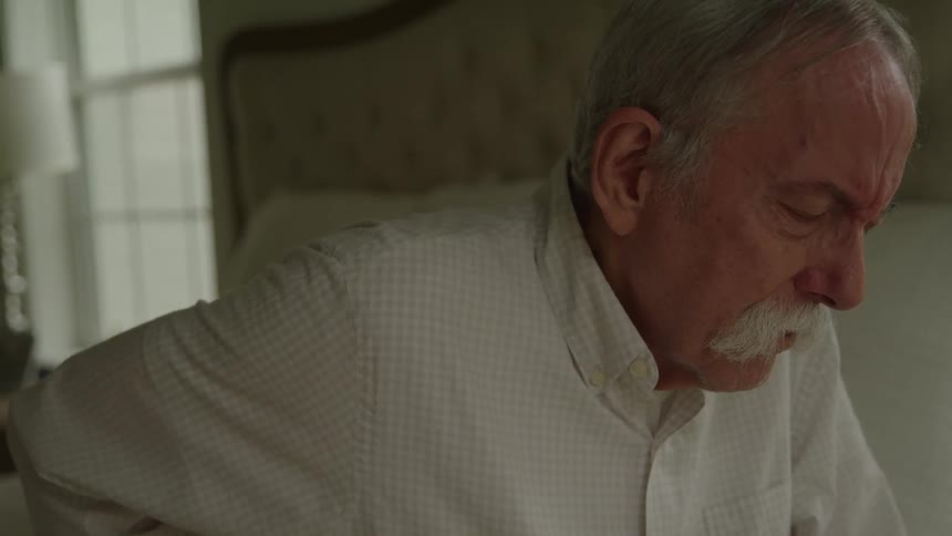 The face of an elderly man with his hand on his back making a pained expression
