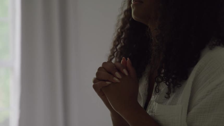 Woman holds her hands together in prayer near the window