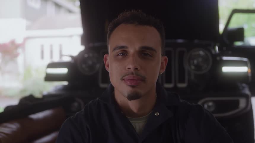 Man with a serious expression in a garage in front of a car