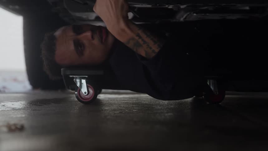 A mechanic on a creeper works on the underside of a car with a wrench