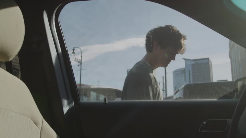 A young man standing next to a locked car throws his hands in the air and rubs his face in distress and frustration