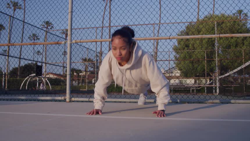 Biracial teenager girl doing push up exercises on a park outdoors during day time