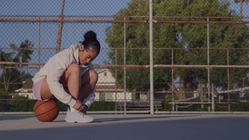 Woman squatting on a basketball court tying her shoelace