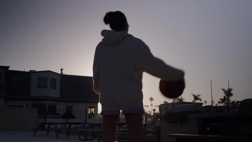 Woman playing with a basketball under the sunset