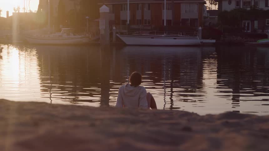 Coastal neighborhood with boats docked as a young man sits near the water