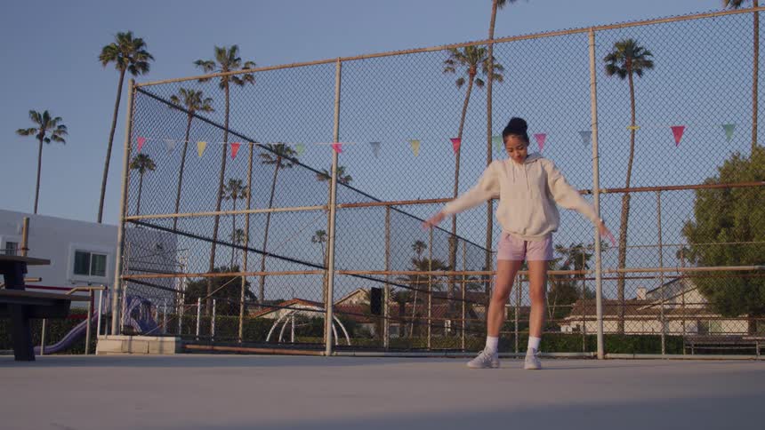 A young woman doing warm up stretches on an open basketball court surrounded by palm trees
