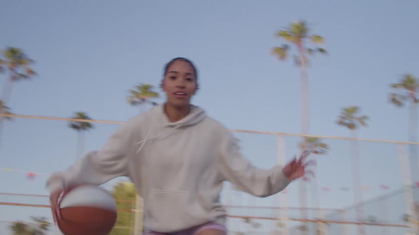 A teenage girl is playing basketball on a court in a city