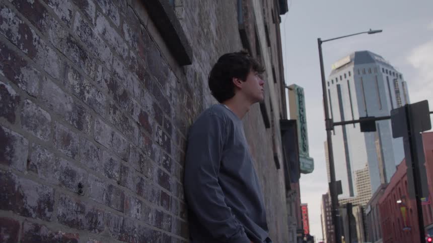 Man leaning against a brick wall watching the city at dusk