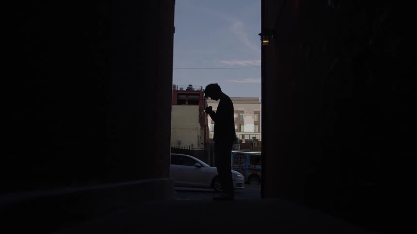 The shadow of a person standing seen from a city alley with cars passing in the background